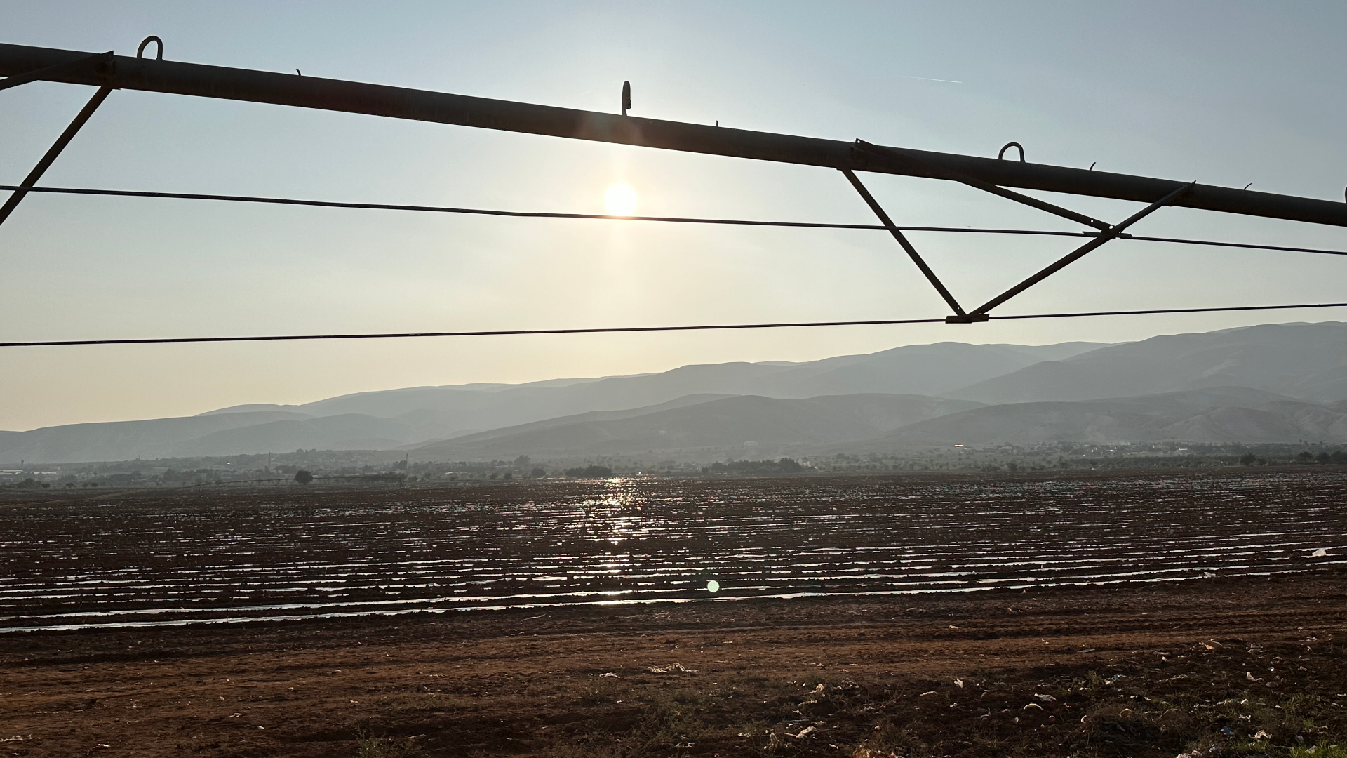 The other side of the watermelon land before seeding — the center-pivot framing the sun over the hills.